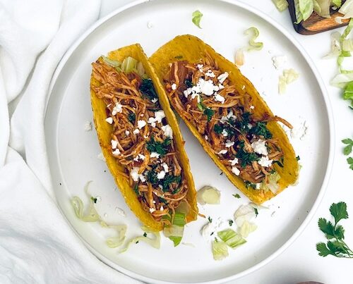 Two crunchy chicken tacos on a plate.