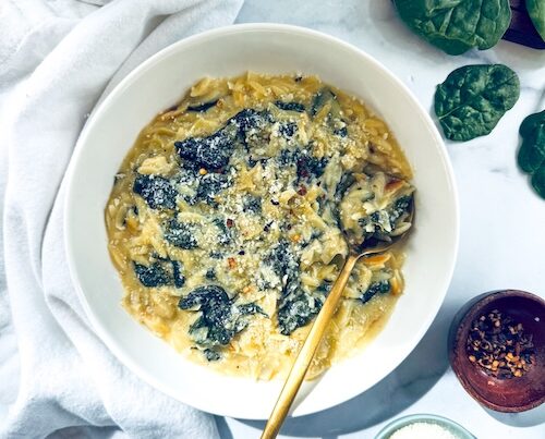 White bowl of spinach artichoke orzo pasta.