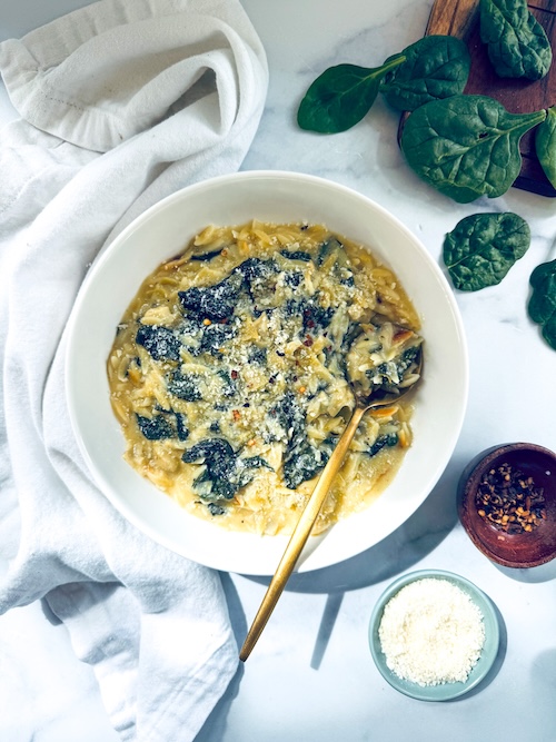White bowl of spinach artichoke orzo pasta.